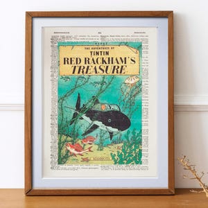 May include: Framed print of a vintage comic book cover, "The Adventures of Tintin: Red Rackham's Treasure." The artwork depicts a submarine shaped like a shark underwater, with fish and seaweed. The background is a dictionary page.