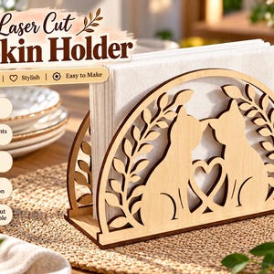 Puede incluir: Un servilletero de madera clara con un diseño cortado a láser de dos gatos frente a frente con un corazón entre ellos, enmarcado por ramas con hojas. El texto Laser Cut Napkin Holder es visible sobre el objeto.