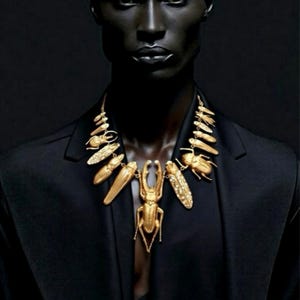Puede incluir: Un collar dorado con colgantes en forma de insectos y elementos decorativos. El collar se lleva sobre una blazer negra, creando un contraste llamativo. El diseño incluye varias formas de escarabajos e insectos, mostrando detalles intrincados.