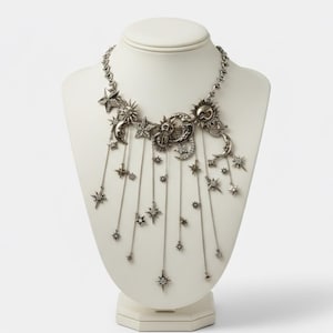 Puede incluir: Collar celestial plateado exhibido en un busto blanco. El collar presenta soles, lunas, estrellas y colgantes de estrella. La cadena es delicada y el diseño es intrincado, creando un accesorio caprichoso y elegante.
