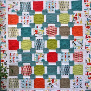 May include: A colorful quilt with a patchwork design featuring various animal prints, geometric patterns, and polka dots. The quilt is made up of squares and rectangles in shades of red, green, blue, and brown.