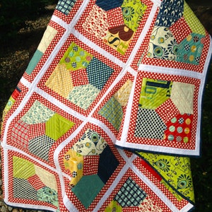 May include: A red, white, and green patchwork quilt with a geometric pattern. The quilt is made of various fabrics with different patterns, including polka dots, leaves, and geometric shapes.