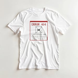 Può includere: Una t-shirt bianca a maniche corte con un riquadro grafico dal bordo rosso contenente il testo ERROR 404, T-SHIRT DESIGN NOT FOUND, e un piccolo testo aggiuntivo che indica che il design cercato non esiste su questa t-shirt.