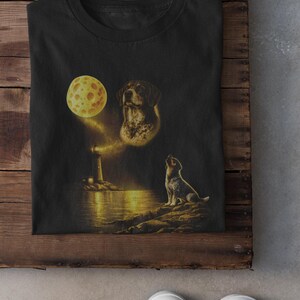 May include: Black t-shirt with a dog-themed graphic. The design depicts a full moon, a lighthouse, and a dog howling at the moon. The graphic is in shades of yellow, brown, and black.