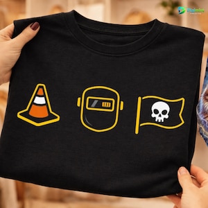 Op de afbeelding: Zwart T-shirt met drie geel omrande afbeeldingen: een verkeerskegel, een lasmasker en een piratenvlag met een schedel. De afbeeldingen zijn gecentreerd op het shirt. Het shirt wordt door handen vastgehouden.