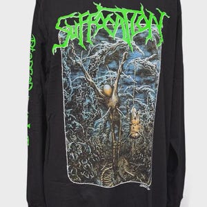 Pode incluir: Uma t-shirt preta de manga comprida com um logótipo verde brilhante que diz Suffocation no topo. O gráfico central retrata uma paisagem escura e surrealista com uma figura esquelética e detalhes intrincados e texturizados em tons de azul e castanho.