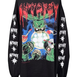 Puede incluir: Una camiseta negra de manga larga con un estampado gráfico de cirujanos con batas verdes realizando una autopsia bajo una luz quirúrgica brillante. La palabra AUTOPSY está impresa en rojo en la parte superior y las mangas tienen estrellas y texto blanco.