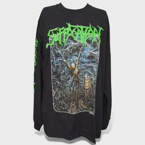 May include: Black long-sleeved shirt with the band name "SUFFOCATION" in neon green, above a detailed, dark illustration. The artwork depicts a skeletal figure in a forest setting. The left sleeve has green text.