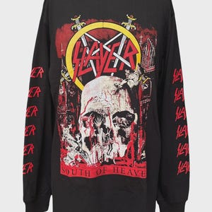 Puede incluir: Una camiseta negra de manga larga con un estampado gráfico de una calavera, espadas y el texto "SLAYER" y "SOUTH OF HEAVEN" en rojo y amarillo. Las mangas tienen impresa la palabra "SLAYER" en color rojo repetida a lo largo de cada brazo.