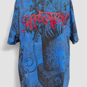 Pode incluir: Uma t-shirt de manga curta com uma estampa gráfica azul e preta em toda a peça, apresentando ilustrações complexas, escuras e surrealistas. A palavra SUFFOCATION está impressa no peito numa fonte vermelha, ousada, irregular e texturizada.