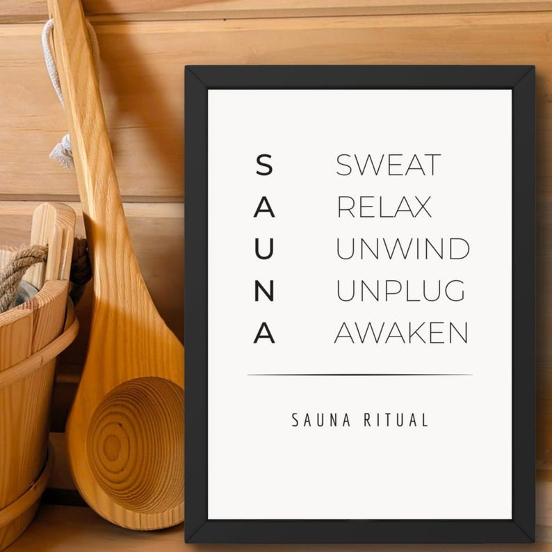 May include: A framed print with the word "SAUNA" stacked vertically on the left and related words on the right: Sweat, Relax, Unwind, Unplug, Awaken. Below the words is the text "SAUNA RITUAL". A wooden sauna bucket and ladle are visible.