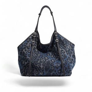 May include: A large tote bag with a blue and gray leopard print pattern. The bag has black leather handles and straps with silver-colored buckles. The bag is designed with a wide opening and a structured shape.