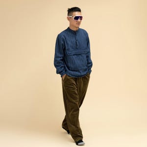 May include: A person wearing a blue striped long-sleeve shirt with a small pocket and brown corduroy pants. The person is also wearing white-framed sunglasses with purple lenses.