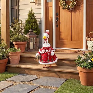 May include: A decorative goose figurine wearing a red and white Christmas-themed outfit, including a matching hat, cape, and dress with white snowflake and green tree patterns. The goose holds a small gift box and a red mug in its wings.
