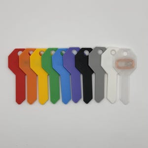 Puede incluir: Una colección de diez llaves en blanco de colores dispuestas en fila. Las llaves son de varios colores, incluyendo rojo, naranja, amarillo, verde, azul, morado, negro, gris, blanco y una llave translúcida con un componente color cobre.