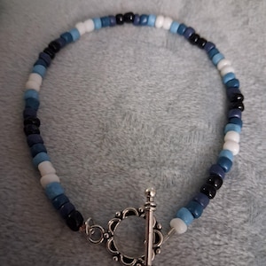 Puede incluir: Pulsera de cuentas con una mezcla de cuentas azules, blancas y negras. Tiene un cierre de palanca plateado. Las pequeñas cuentas redondas crean un accesorio delicado. Aproximadamente 17 cm de largo.