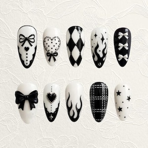 Könnte beinhalten: Ein Set von zehn künstlichen Nägeln mit verschiedenen schwarz-weißen Designs. Die Designs umfassen Schleifen, Herzen, Flammen, Rauten und Sterne. Die Nägel sind oval geformt und haben ein glänzendes Finish.