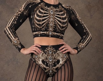 May include: A black long-sleeve crop top and high-waisted briefs set featuring a detailed gold and white skeletal rib cage print with ornate embellishments, paired with black vertical striped tights and black lace-up platform ankle boots.