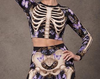 May include: A long-sleeved crop top and matching leggings set featuring a black base with a printed human skeleton rib cage and pelvic bone design. The fabric is decorated with purple butterflies and clusters of small purple flowers throughout.