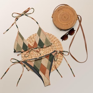 Puede incluir: Un conjunto de bikini de dos piezas con un patrón de rombos en tonos verde oliva, terracota y beige. El conjunto incluye un top triangular con tiras para atar y una braguita a juego con lazos laterales. Incluye un bolso redondo trenzado y gafas.