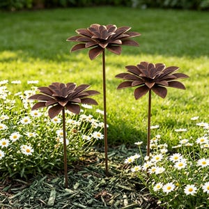 May include: Three decorative metal flower garden stakes with layered petal designs. The stakes are a dark brown color and are placed in a garden bed with white flowers and green grass in the background. The stakes vary in height.