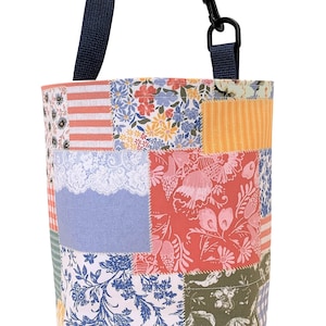 K&ouml;nnte beinhalten: Eine Patchwork-Tragetasche mit einem blauen Trageriemen. Die Tasche besteht aus verschiedenen Stoffen mit floralen und geometrischen Mustern in den Farben Rosa, Blau, Gr&uuml;n und Gelb.