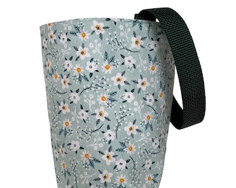 May include: A fabric tote bag with a floral pattern. The bag features a light green background with white flowers and yellow centers. A dark green strap is attached to the side of the bag.