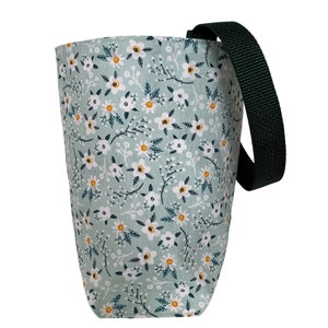 May include: A fabric tote bag with a floral pattern. The bag features a light green background with white flowers and yellow centers. A dark green strap is attached to the side of the bag.