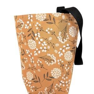 May include: A fabric tote bag with a floral pattern. The bag is a mustard yellow color with a repeating pattern of white flowers and black stems and leaves. It has a black strap for carrying.
