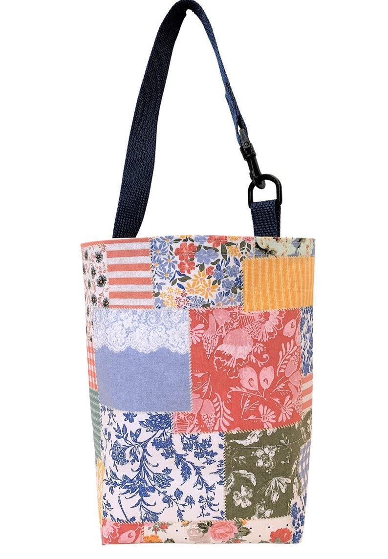 K&ouml;nnte beinhalten: Eine Patchwork-Tragetasche mit einem blauen Trageriemen. Die Tasche besteht aus verschiedenen Stoffen mit floralen und geometrischen Mustern in den Farben Rosa, Blau, Gr&uuml;n und Gelb.