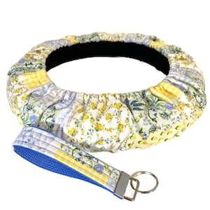 May include: A floral patterned steering wheel cover and matching key fob. The cover features a patchwork design with yellow, blue, and white floral prints. The key fob has a blue strap and silver hardware.