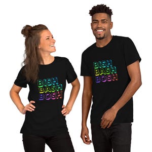 Puede incluir: Dos personas vistiendo camisetas negras con el texto "BISH BASH BOSH" en degradado arcoíris. Las camisetas son de manga corta y parecen estar hechas de un material suave. Las personas están sonriendo.