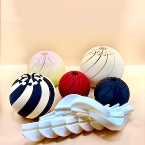May include: An assortment of decorative spheres in various colors, including white, red, navy, and a black and white striped design. A white, segmented, curved object is in the foreground. The spheres have a textured, ribbed design.