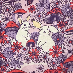 May include: A fabric pattern featuring white rabbits, red mushrooms, and various flowers in shades of purple, red, and white. The design has a whimsical, vintage aesthetic, with a repeating floral and fauna motif.