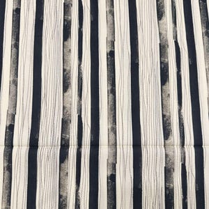 以下が含まれることがあります： 縦縞模様の生地のクローズアップ。ネイビーブルー、白、グレーのストライプが交互に配置され、テクスチャードデザインを作り出しています。白いストライプには細い点線があり、テキスタイルに詳細を追加しています。