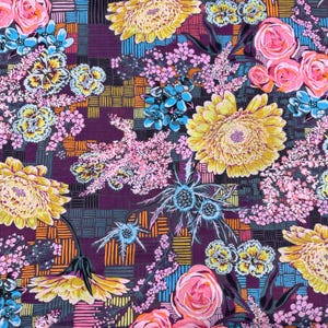 May include: A purple fabric with a repeating pattern of yellow, pink, and blue flowers. The flowers are arranged in a checkered pattern with orange and blue lines.