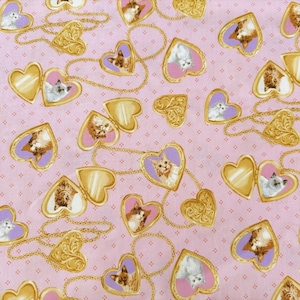 May include: A light pink fabric featuring a repeating pattern of gold-colored heart-shaped lockets connected by thin gold chains. Each locket contains a small portrait of a cat against a purple background. The fabric has a subtle grid of dots.