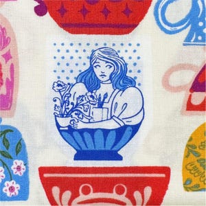 May include: A fabric pattern featuring a central illustration of a woman with blue hair holding flowers in a blue bowl. The design includes red, blue, and yellow bowls and floral motifs on a white background.