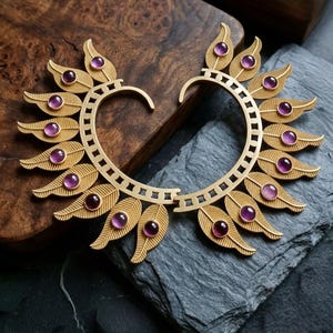 May include: Gold-toned ear cuffs with leaf and gemstone design. Each cuff features a series of stylized leaves, each adorned with a round, purple gemstone. The cuffs are set against a dark, textured background.