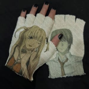 Puede incluir: Guantes sin dedos de punto blanco roto con estampados de personajes de anime. Un guante muestra a una mujer rubia guiñando un ojo, el otro a un hombre con pelo gris. Los guantes tienen un borde deshilachado y desgastado.