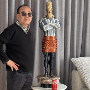 May include: A detailed statue of a muscular figure with a golden headdress, silver torso, and a copper-colored skirt. The statue is standing on a small, round table with a can of Coca-Cola. The statue is approximately 30 inches tall.