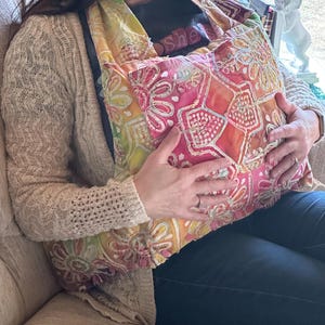 Puede incluir: Una almohada de tela colorida y estampada con un diseño floral. La almohada está hecha de un material suave y ligero y tiene un aspecto único, cosido a mano.