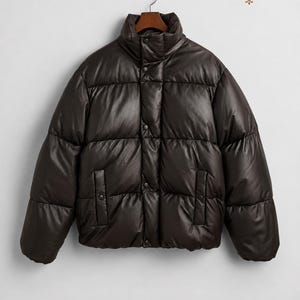 May include: A dark brown puffer jacket with a high collar, long sleeves, and a front button closure. The jacket features a quilted design with horizontal panels and two side pockets. The text LEATHERMINEART is visible in the top right corner.