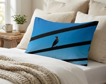 May include: A rectangular pillowcase featuring a vibrant blue sky background with three thick, horizontal black lines crossing the surface. A small, dark bird is perched on the center black line, facing toward the left side of the pillowcase.
