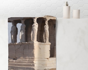 May include: A bath towel featuring a detailed illustration of the Erechtheion, an ancient Greek temple. The artwork depicts the Caryatids, sculpted female figures, supporting the structure's roof. The towel is beige and white, with a classic architectural theme.