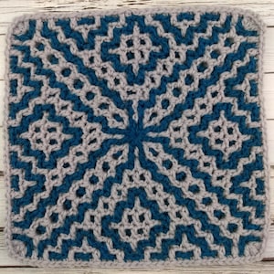 Puede incluir: Un cuadrado de granny al crochet con un patrón geométrico en azul verdoso y gris.