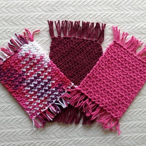 May include: Three crocheted pot holders with fringe. One is pink, one is burgundy, and one is a multi-colored pink and white pattern.