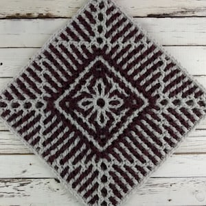 May include: A square crochet granny square with a central flower design in burgundy and a border in gray. The square is made with a textured stitch pattern.