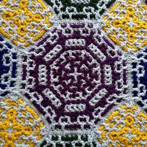 May include: A close-up of a crocheted blanket with a repeating geometric pattern in shades of blue, yellow, purple, and green.