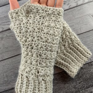 Op de afbeelding: Een paar beige gebreide vingerloze handschoenen met een textuurpatroon. De handschoenen zijn gemaakt van zacht garen en hebben een comfortabele pasvorm.